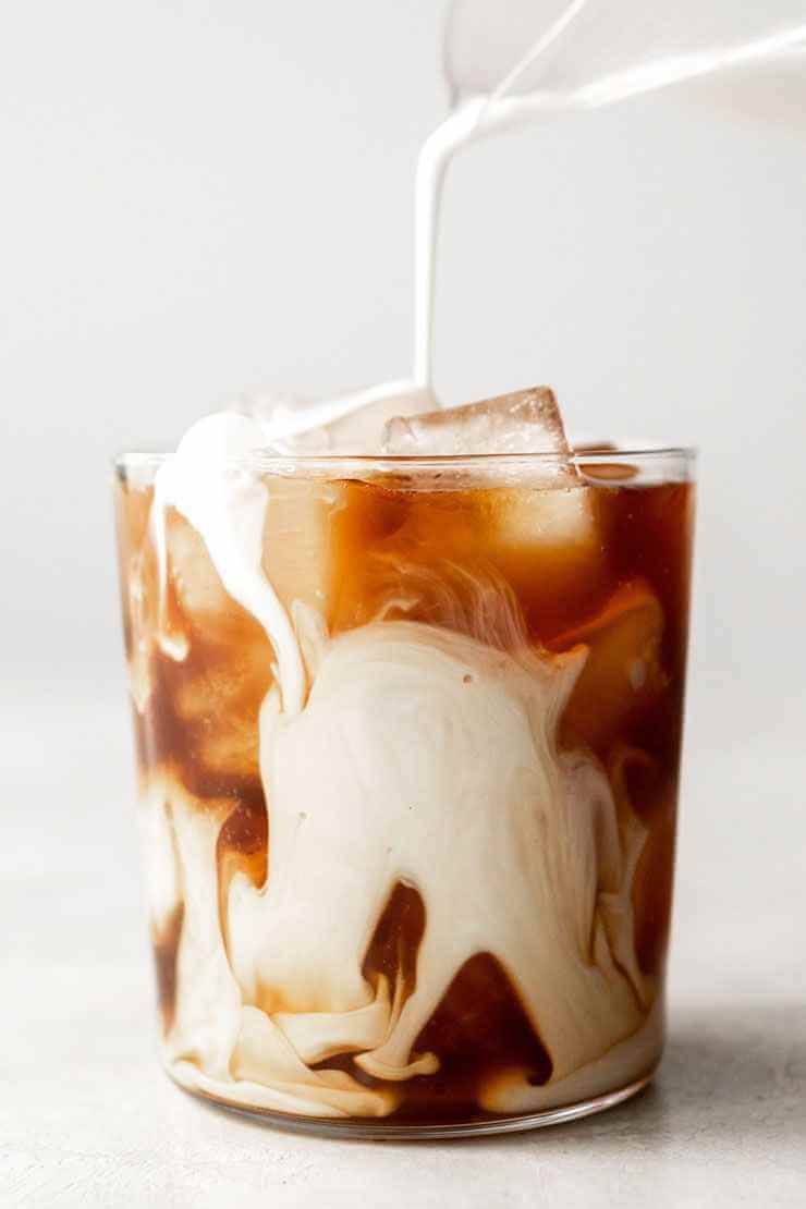 Слоистый латте CoffeBrew в стеклянном стакане среди зелени